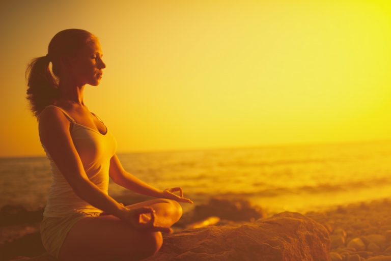 woman sitting in lotus position at sunset on beach shoreline